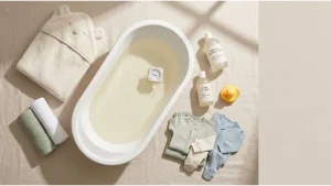 how to bathe your baby — essential bathing tools laid out, including baby bath tub, soft washcloth, hooded towel, and gentle baby soap on a clean surface